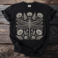 Black t-shirt with a detailed cream line art dragonfly surrounded by daisies and ferns.