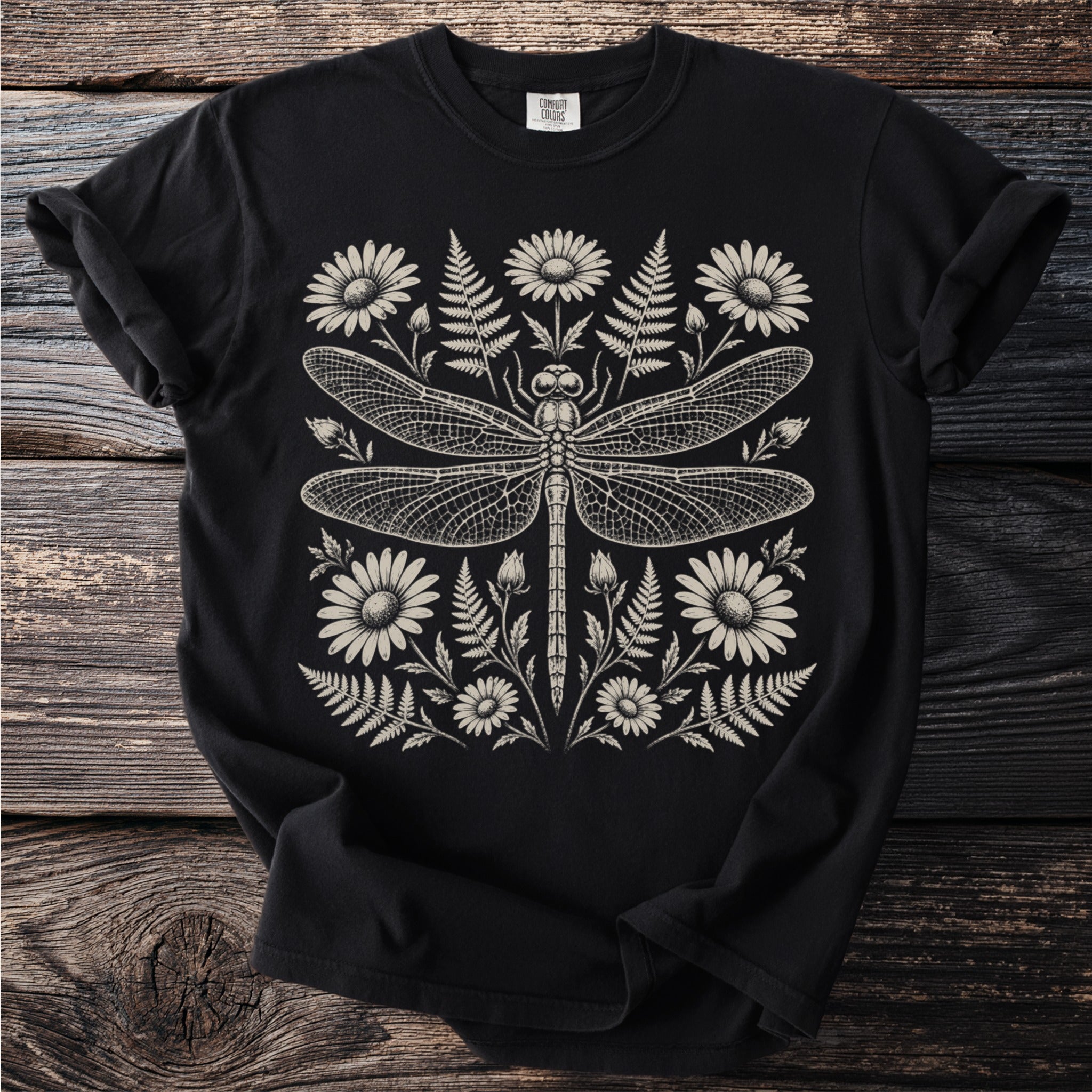 Black t-shirt with a detailed cream line art dragonfly surrounded by daisies and ferns.