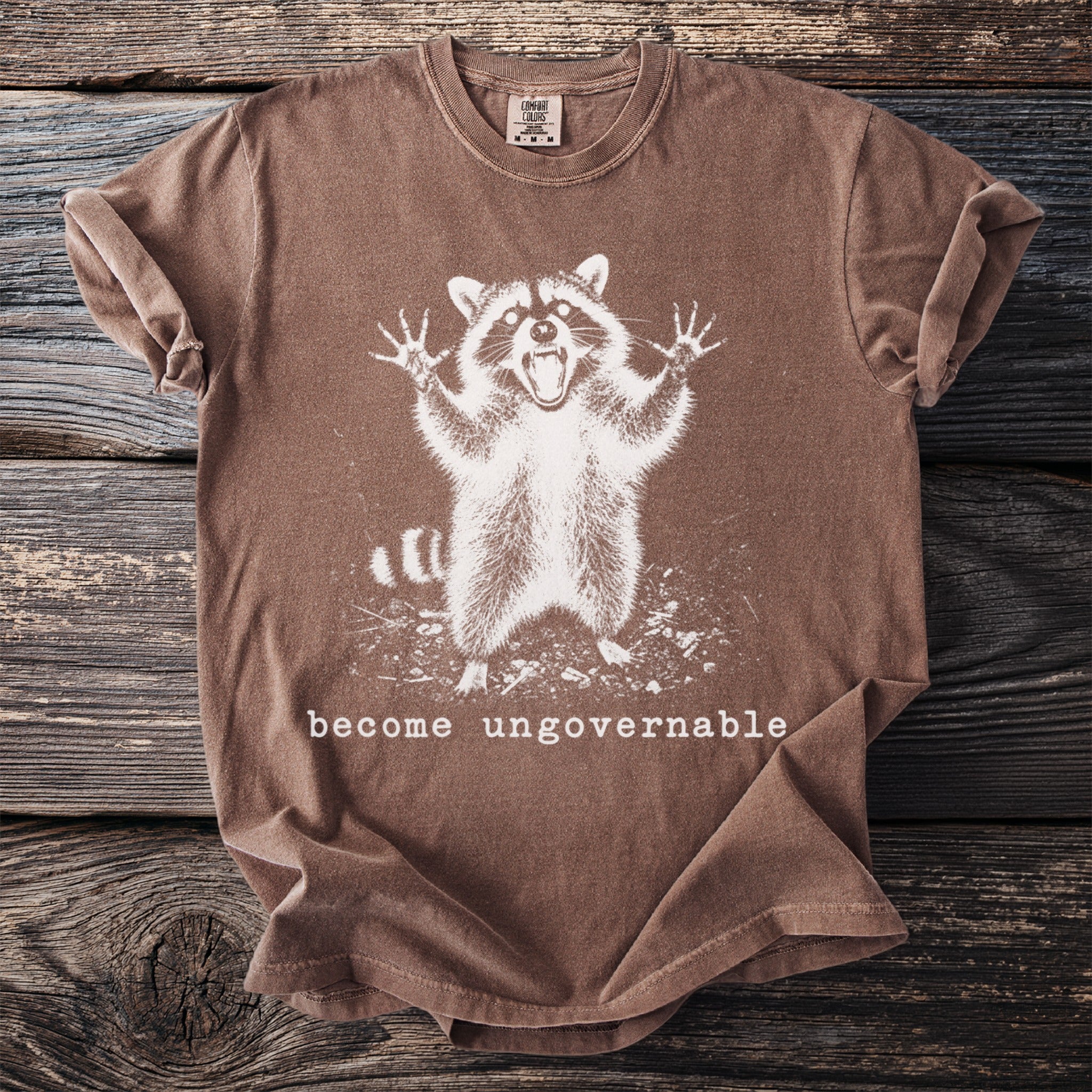 Brown t-shirt with distressed graphic of a shouting raccoon and text "become ungovernable".