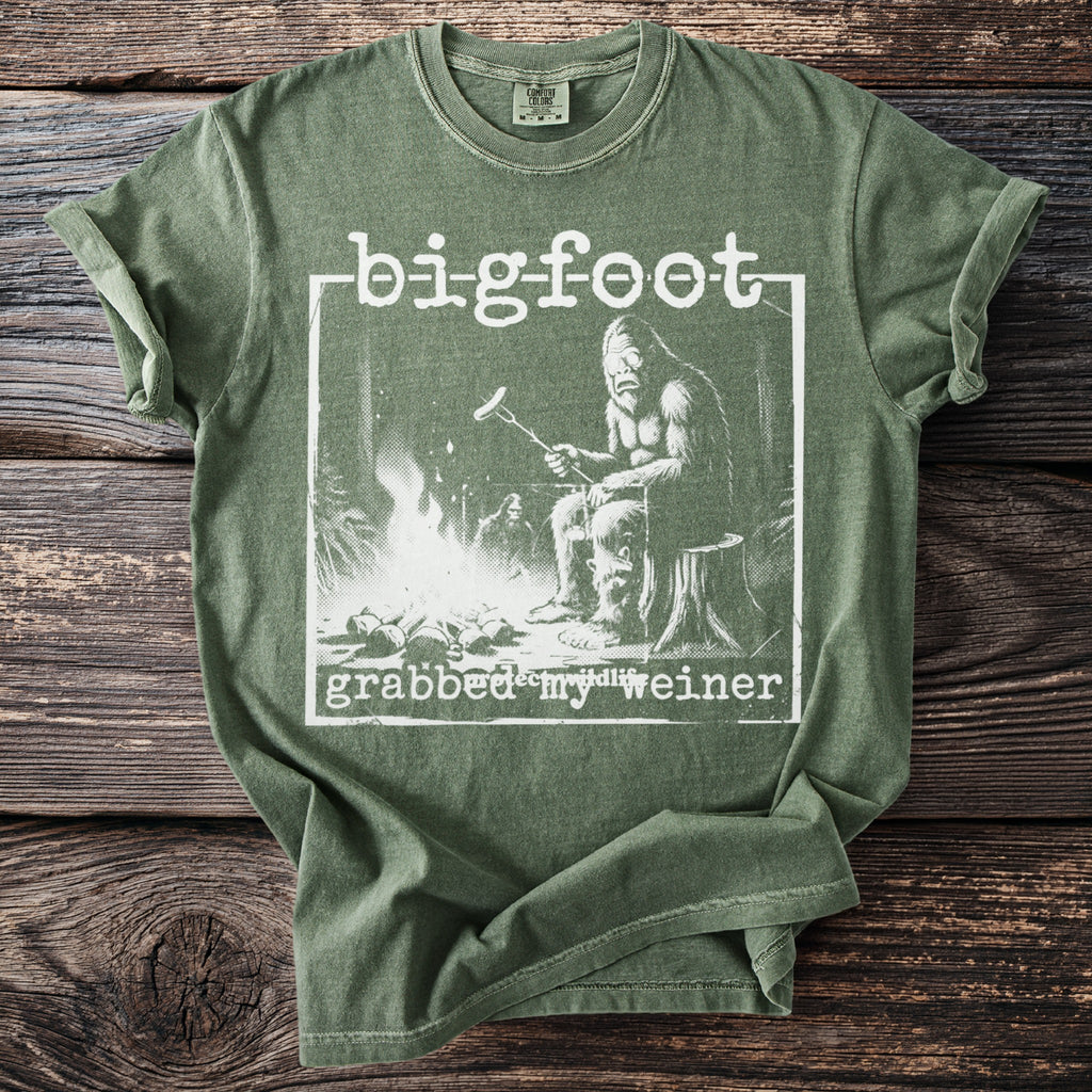 Green t-shirt with Bigfoot sitting by a campfire and the text "bigfoot grabbed my weiner".