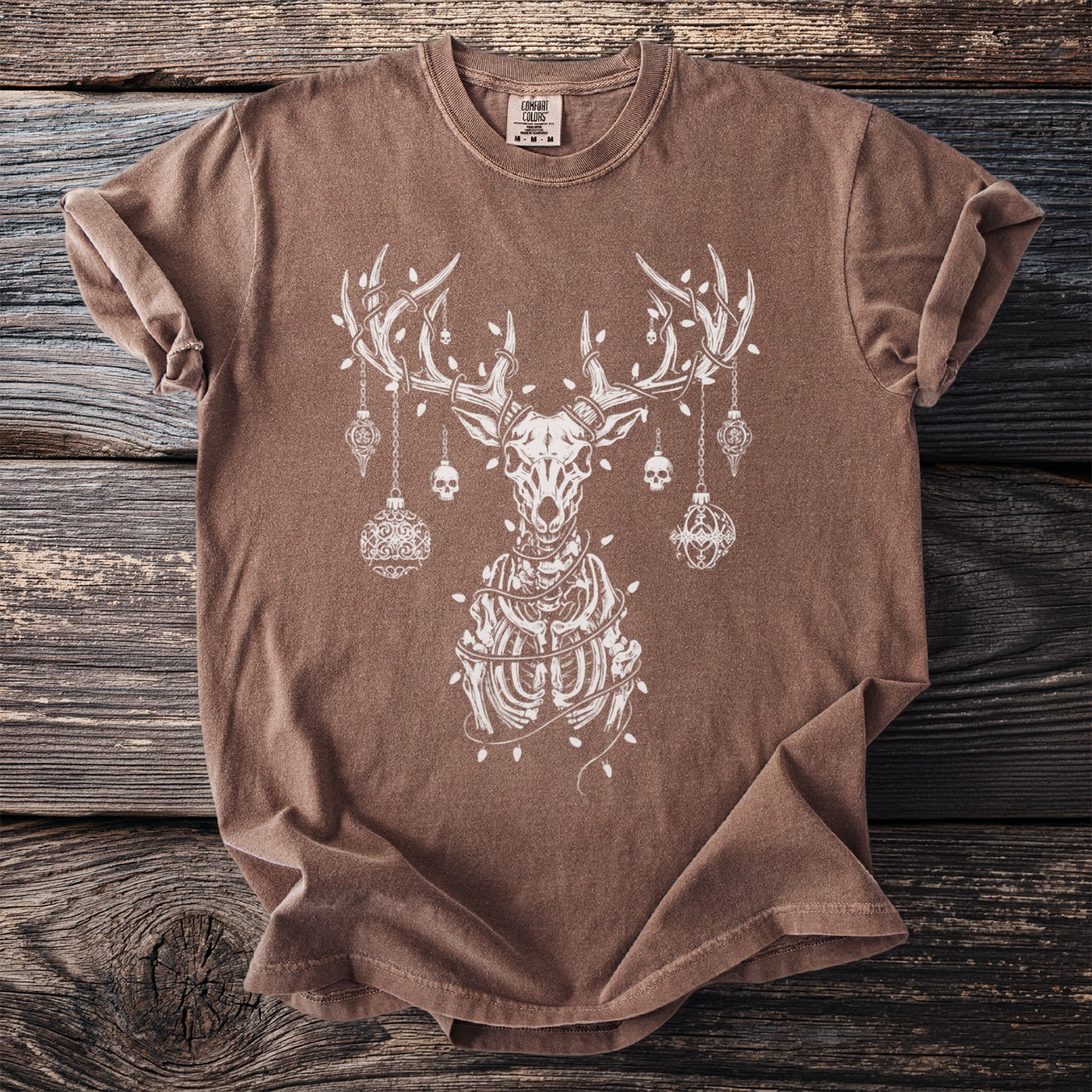 Brown t-shirt with white skeleton deer, ornaments, and Christmas lights graphic.
