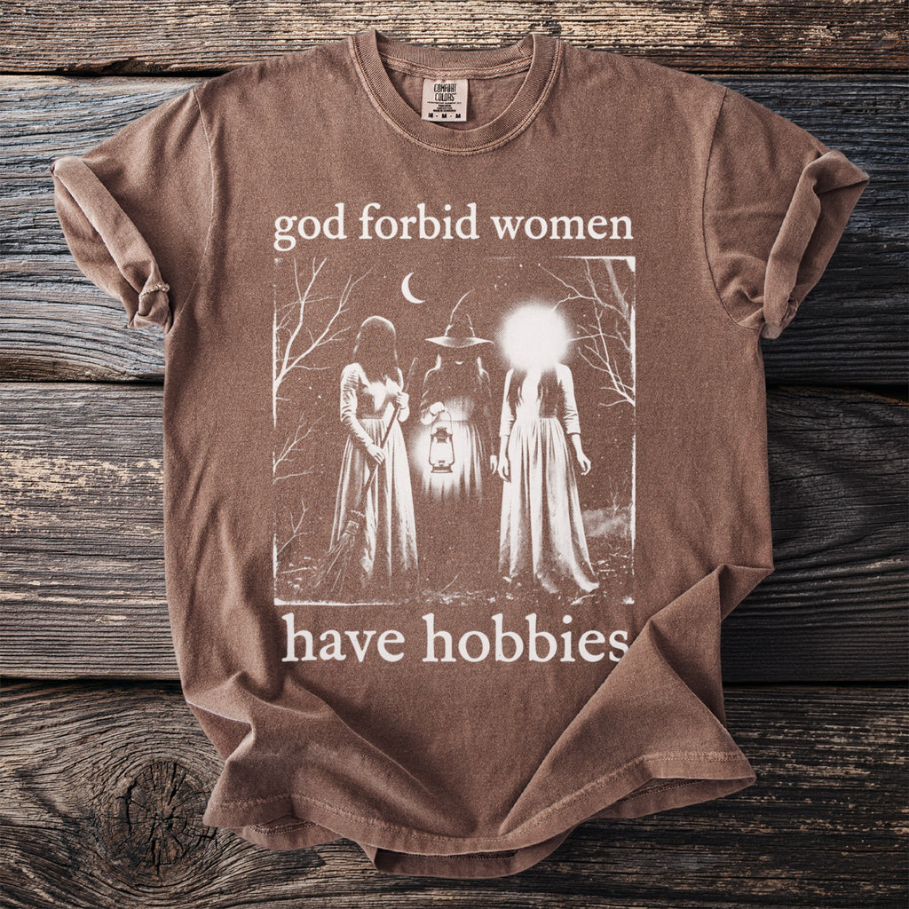 Brown t-shirt with graphic art of three women and text "god forbid women have hobbies".