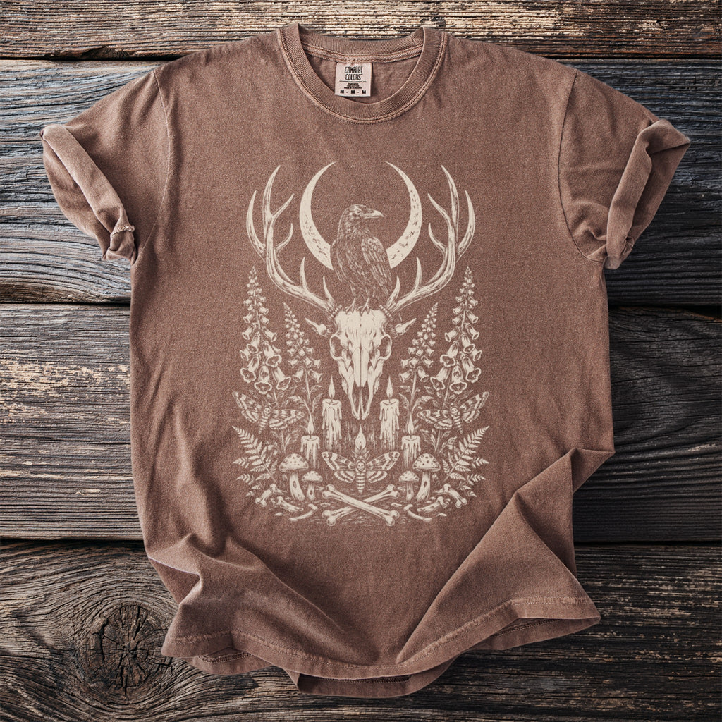Brown t-shirt with a cream graphic of a raven on deer antlers, skull, and occult imagery.