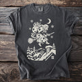 Pepper gray t-shirt with a cream folk-cut print: La Befana flies over snowy rooftops on her broom, a sack of gifts on her back.