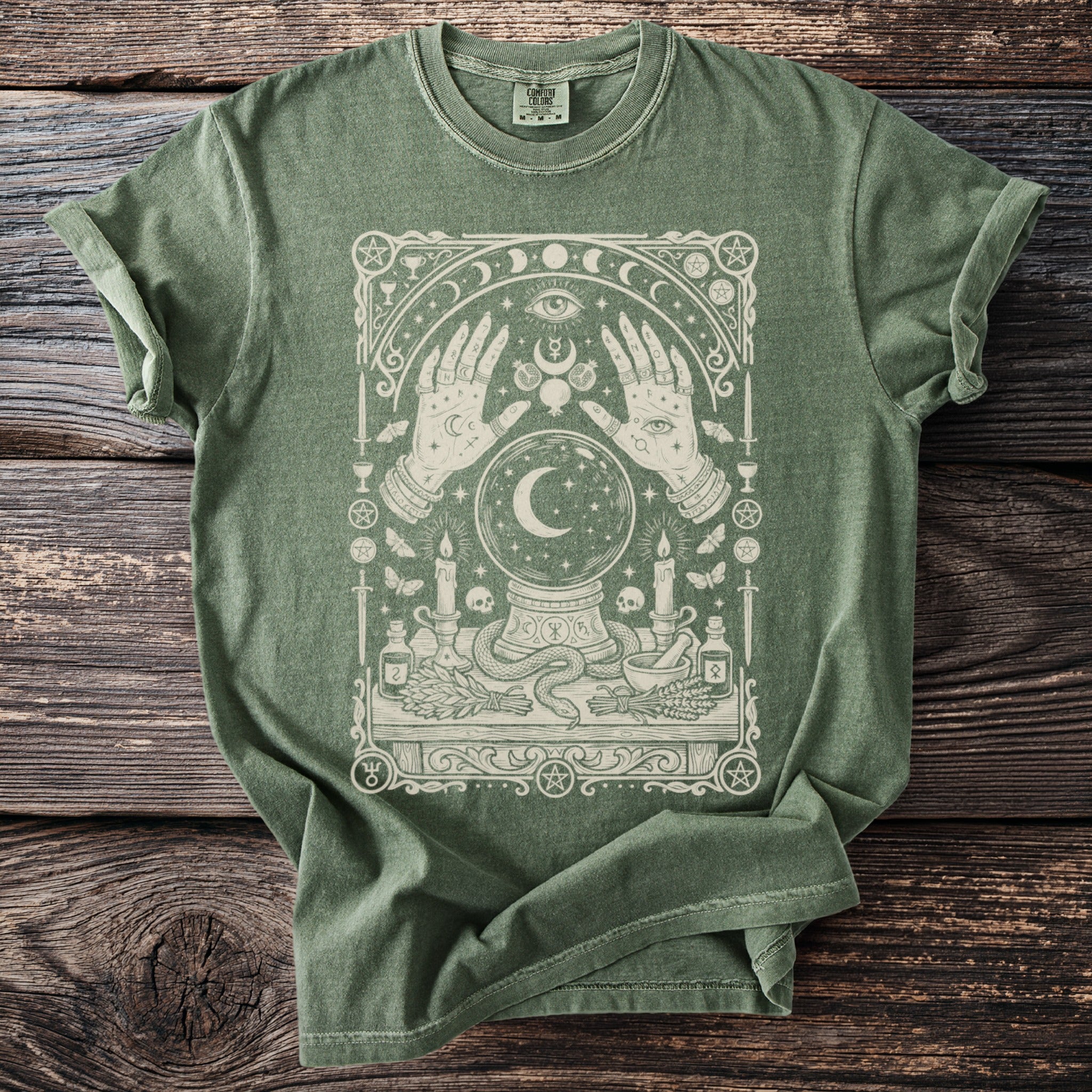 Green t-shirt with arcane illustration of hands, crystal ball, snake, and candles.