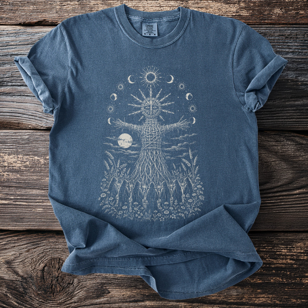Blue t-shirt with a woven figure, sun, moons, and figures in a field.