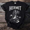 Black t-shirt with white text "HERMIT" and graphic of a robed figure holding a lantern.