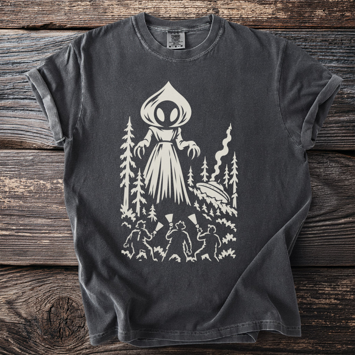 Graphic tee with alien, UFO, trees, and people holding flashlights.