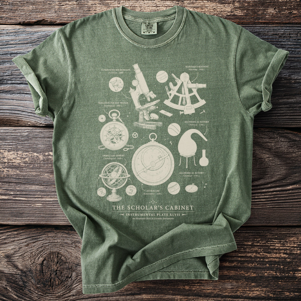 Green t-shirt with cream illustration of scientific instruments including a microscope, sextant, astrolabe, and pocket watch.
