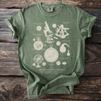 Green t-shirt with cream illustration of scientific instruments including a microscope, sextant, astrolabe, and pocket watch.