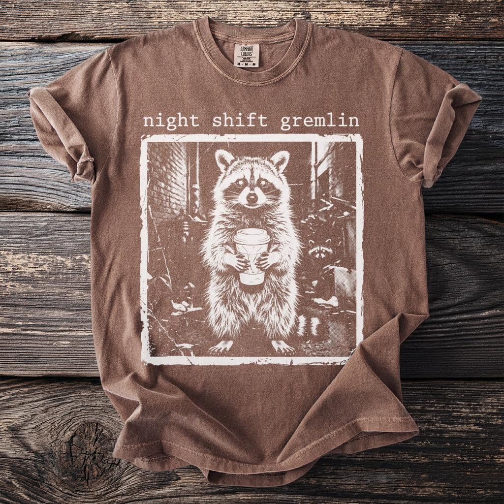 Brown t-shirt with "night shift gremlin" and raccoon holding coffee mug graphic.