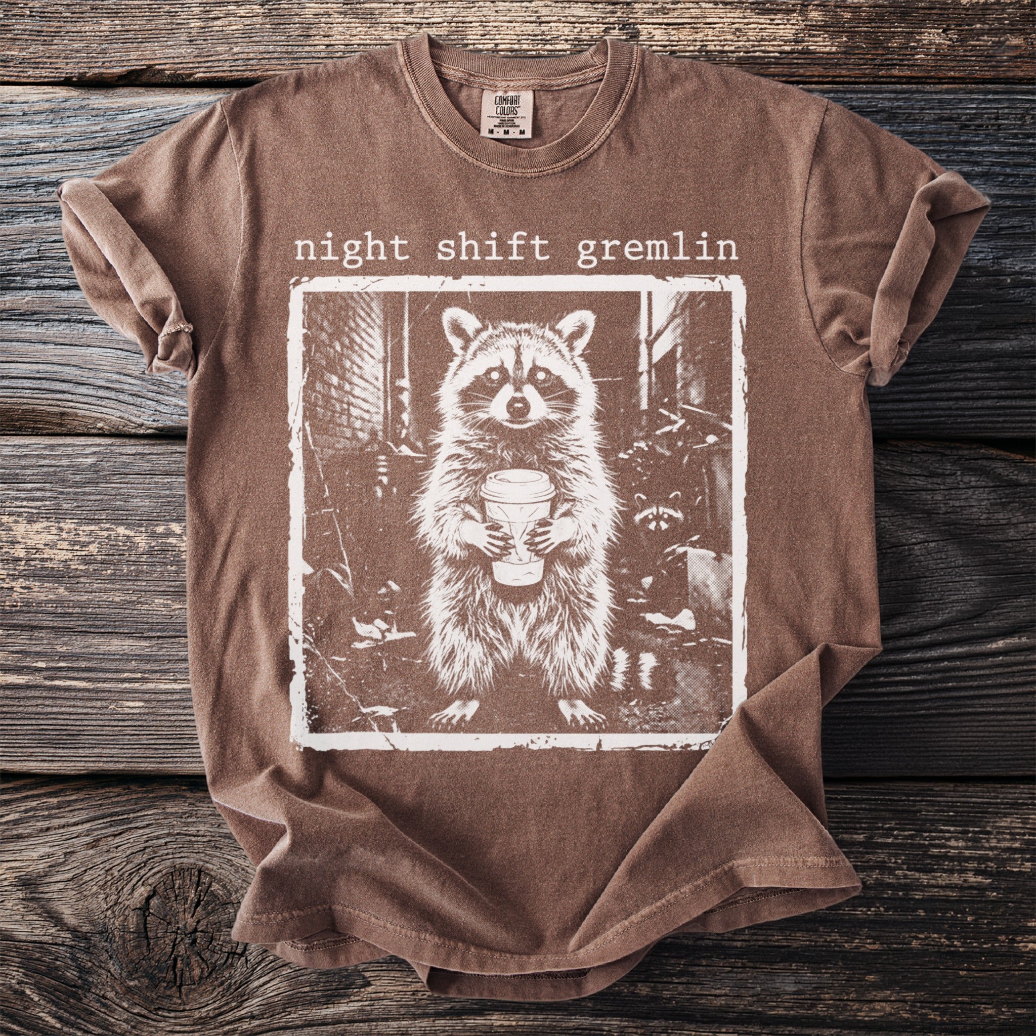 Brown t-shirt with "night shift gremlin" and raccoon holding coffee mug graphic.