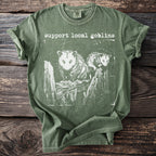 Comfort Colors green t-shirt with "support local goblins" and opossums on a fence.