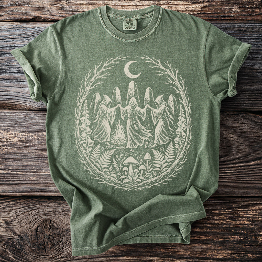 Green t-shirt featuring a light graphic of robed figures dancing around a fire under a moon.