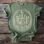 Green t-shirt featuring a light graphic of robed figures dancing around a fire under a moon.
