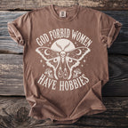 Brown t-shirt with text "God Forbid Women Have Hobbies" and moth graphic.