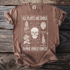 Brown t-shirt featuring skull and toxic plants with text: "ALL PLANTS ARE EDIBLE, SOME ONLY ONCE".