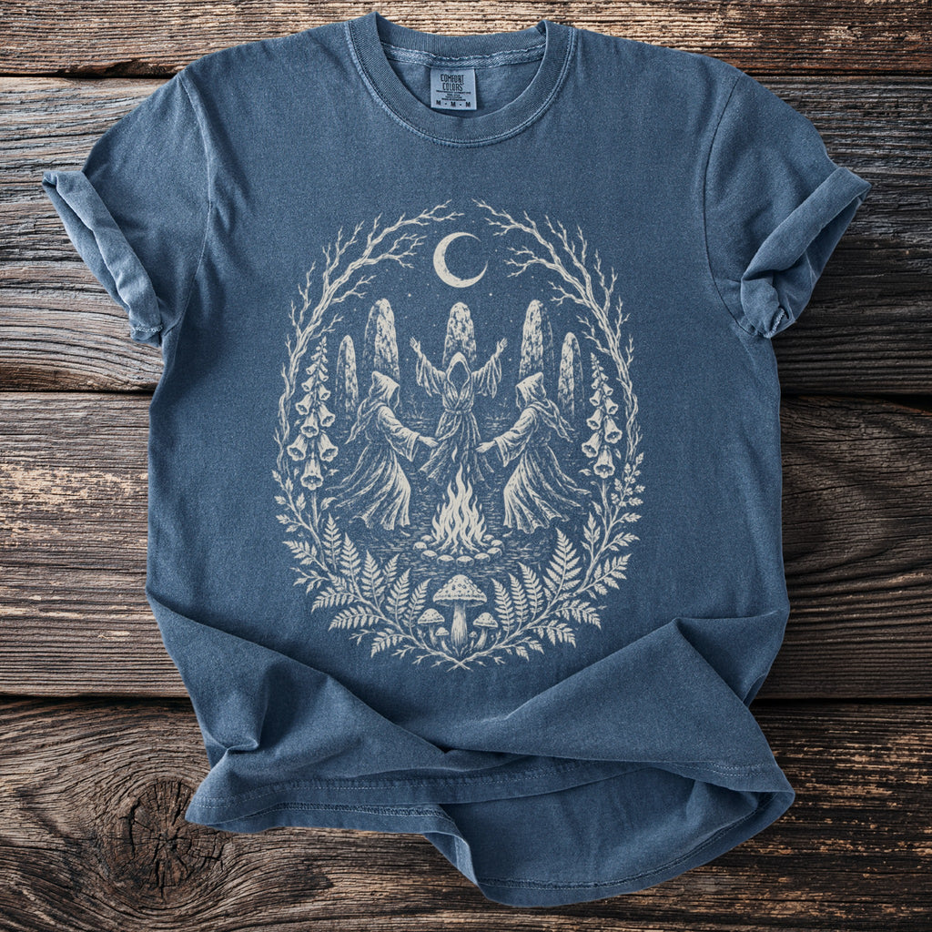 Blue t-shirt with a white illustration of figures dancing around a bonfire under a moon.