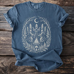 Blue t-shirt with a white illustration of figures dancing around a bonfire under a moon.