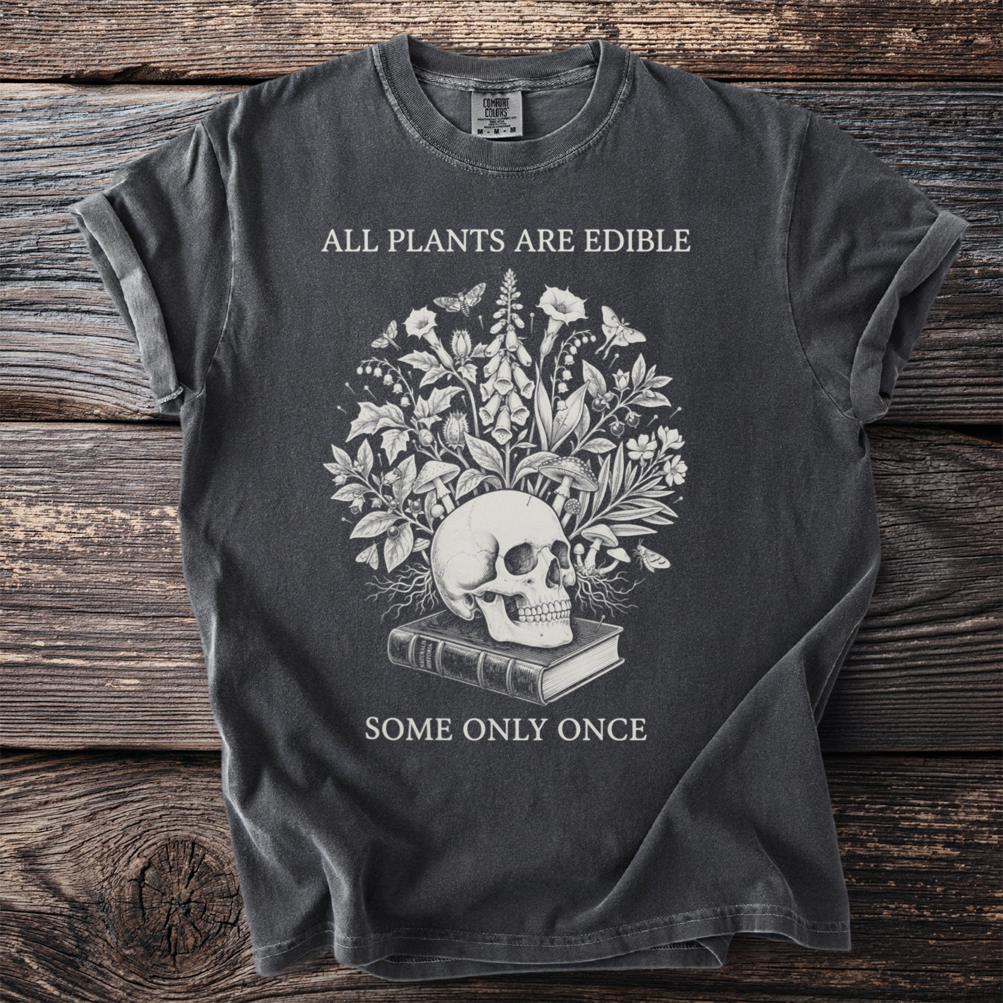 Dark t-shirt with skull, plants, and text "ALL PLANTS ARE EDIBLE SOME ONLY ONCE".