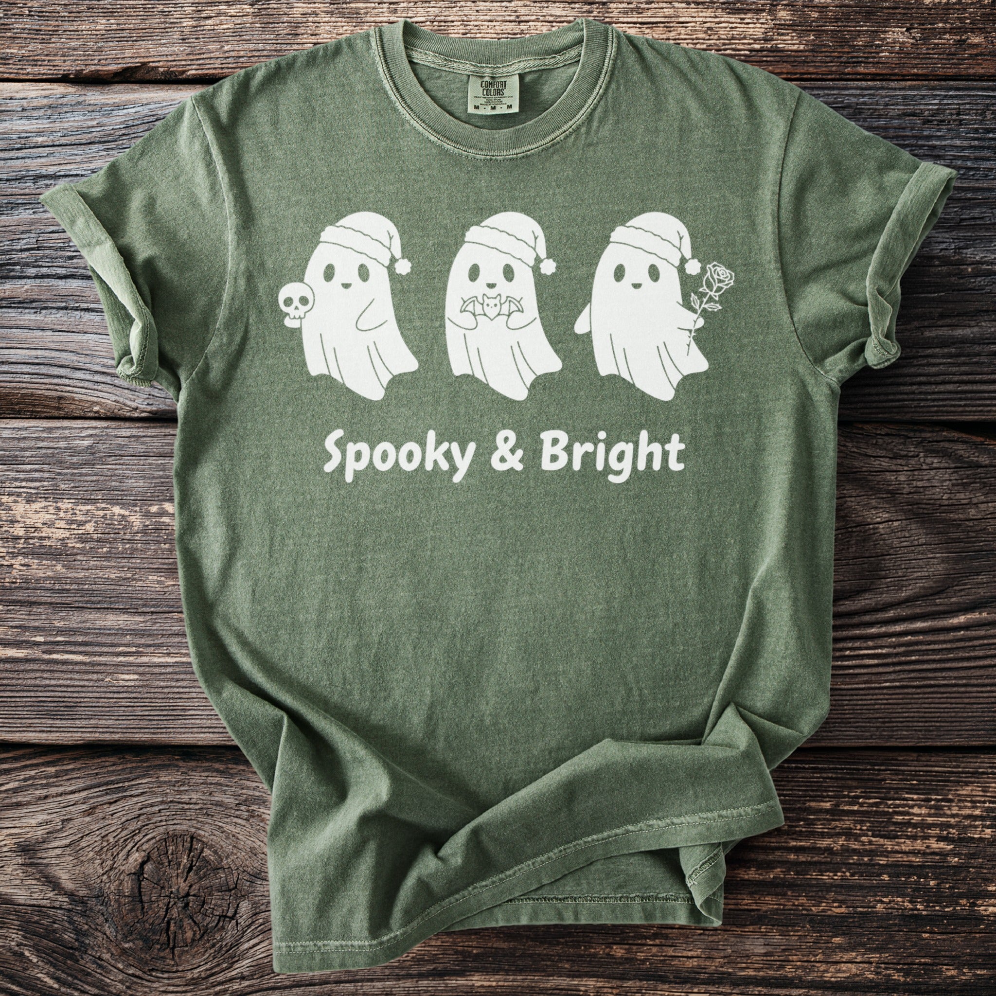 Green t-shirt with three white ghosts wearing Santa hats and text "Spooky & Bright".