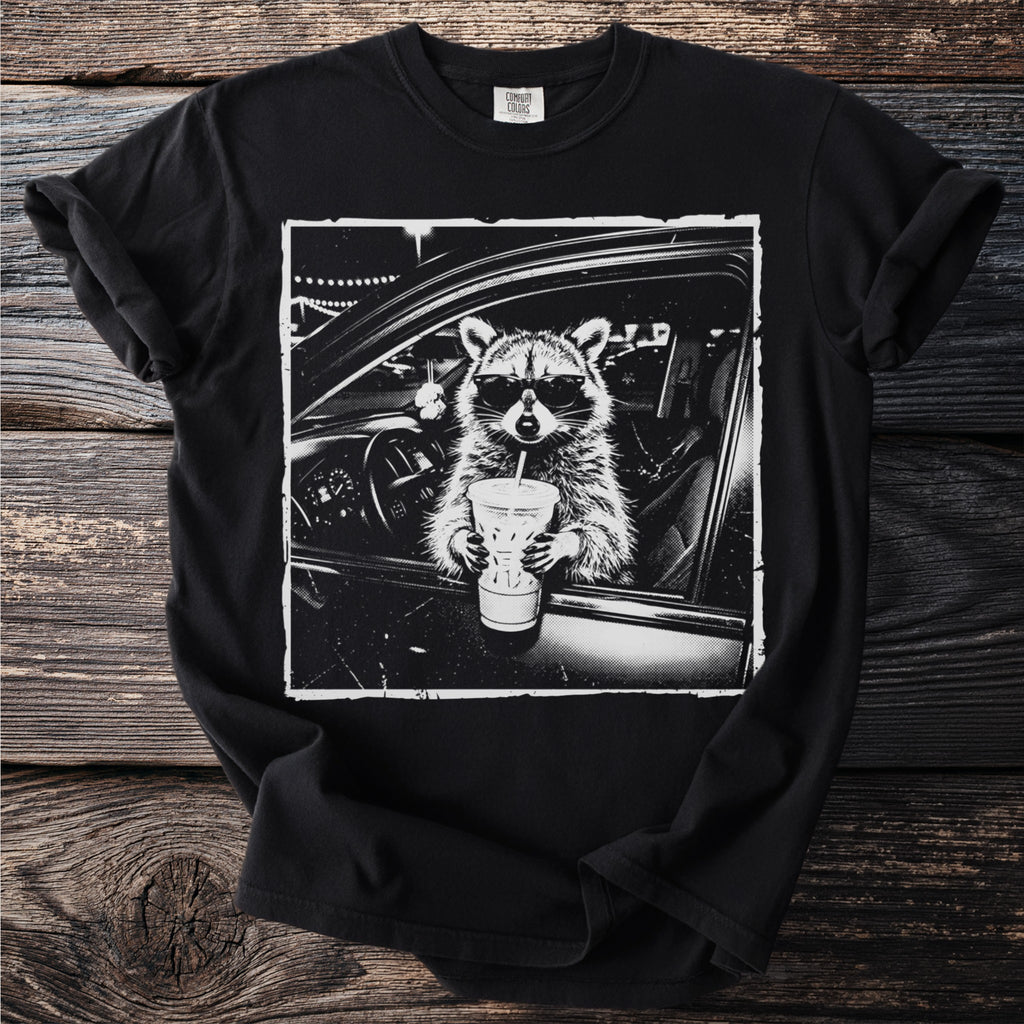 Black t-shirt with a raccoon wearing sunglasses in a car holding a drink.