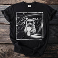 Black t-shirt with a raccoon wearing sunglasses in a car holding a drink.