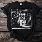 Black t-shirt with a raccoon wearing sunglasses in a car holding a drink.