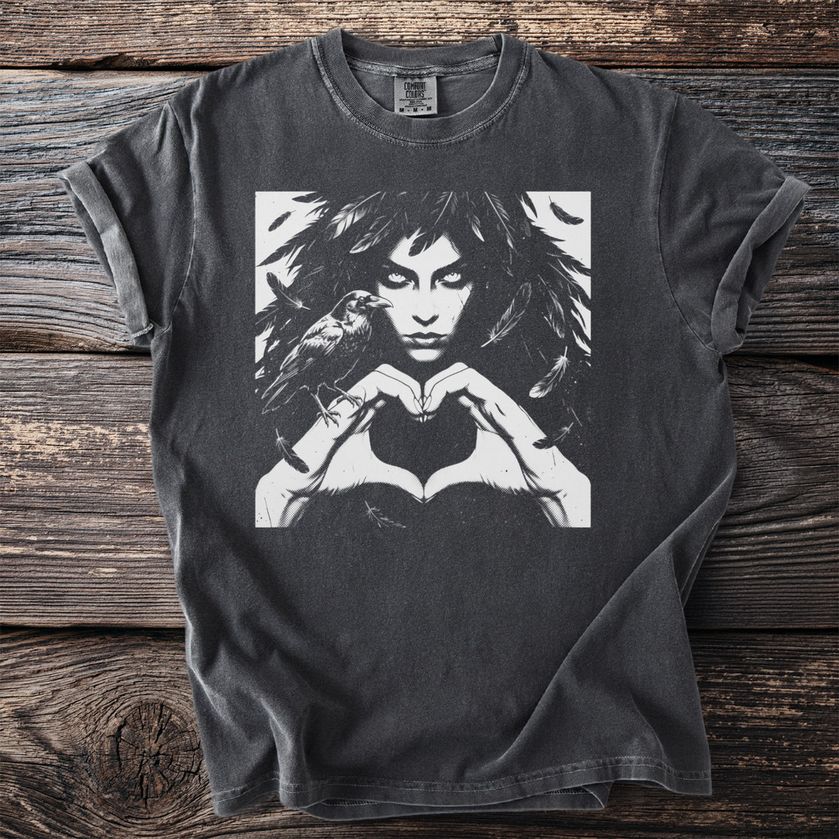 The Morrigan Heart Hands design on a pepper grey t-shirt: a feather-haired woman forming a heart with her hands, a raven perched on her wrist.