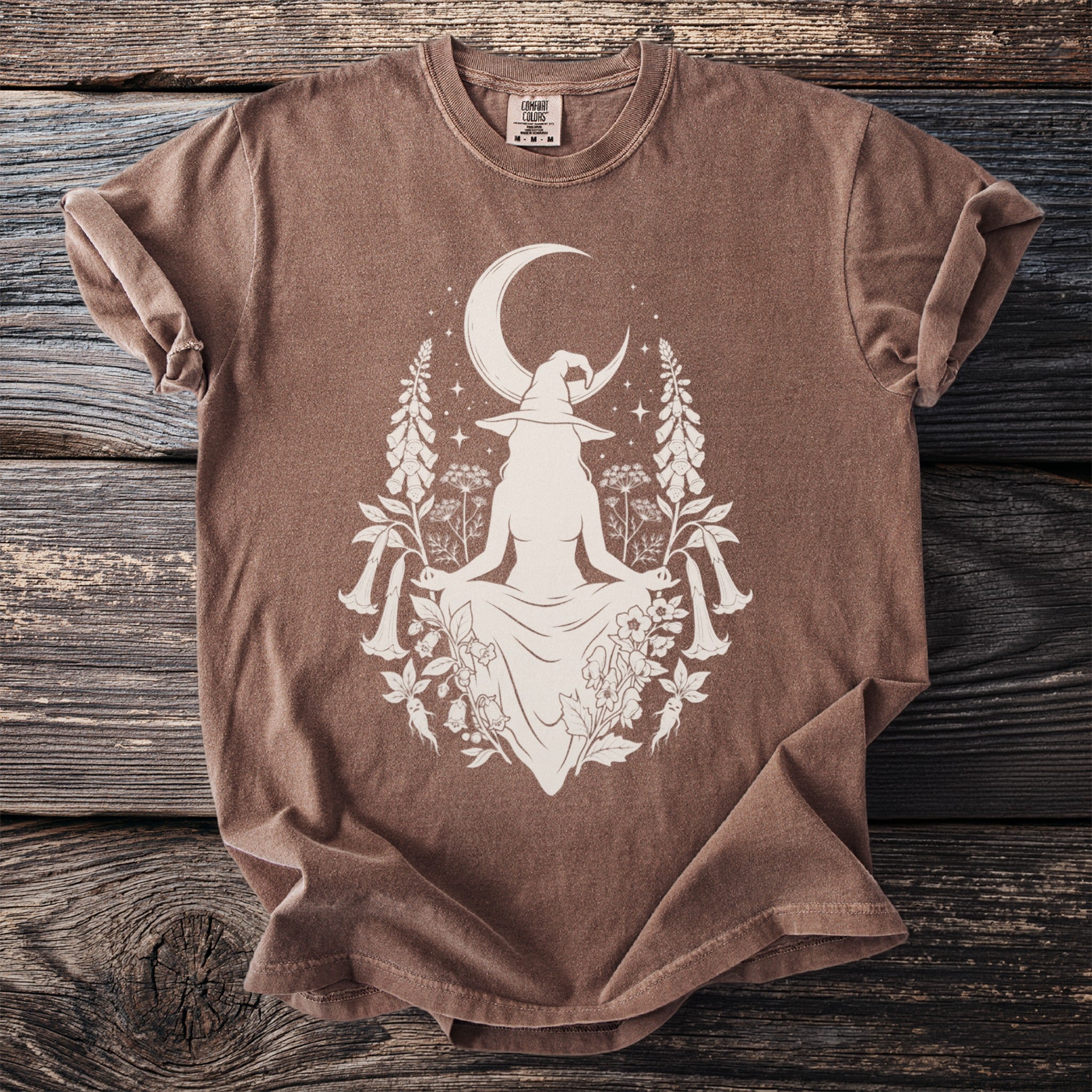 Brown t-shirt with white witch silhouette, crescent moon, and floral elements.