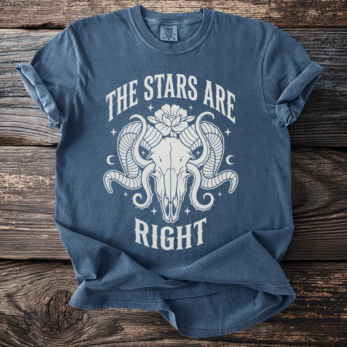 Blue t-shirt with white graphic of ram skull, flower, and text "THE STARS ARE RIGHT".