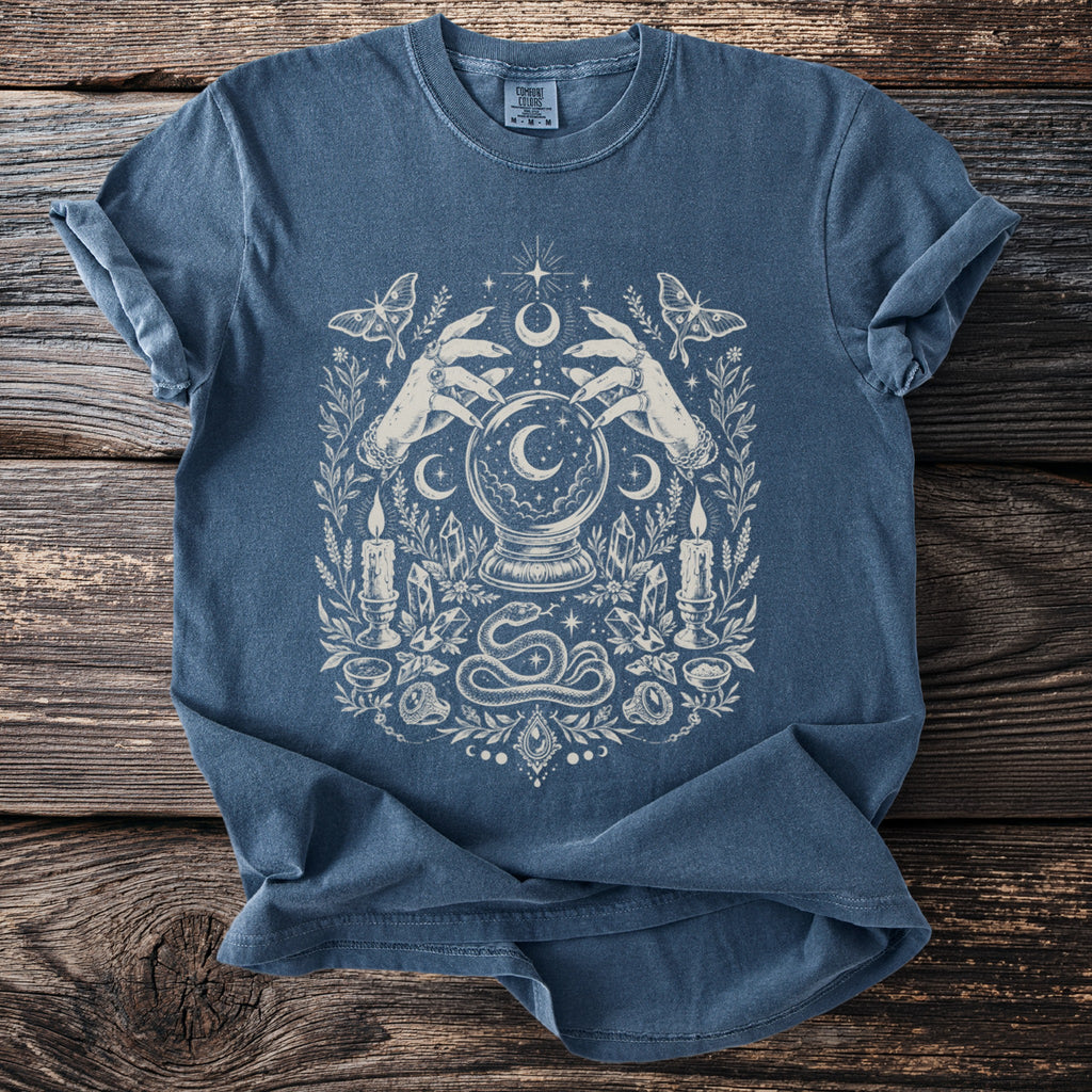 Blue t-shirt with mystical graphic featuring hands, crystal ball, snake, moths, candles, and crystals.