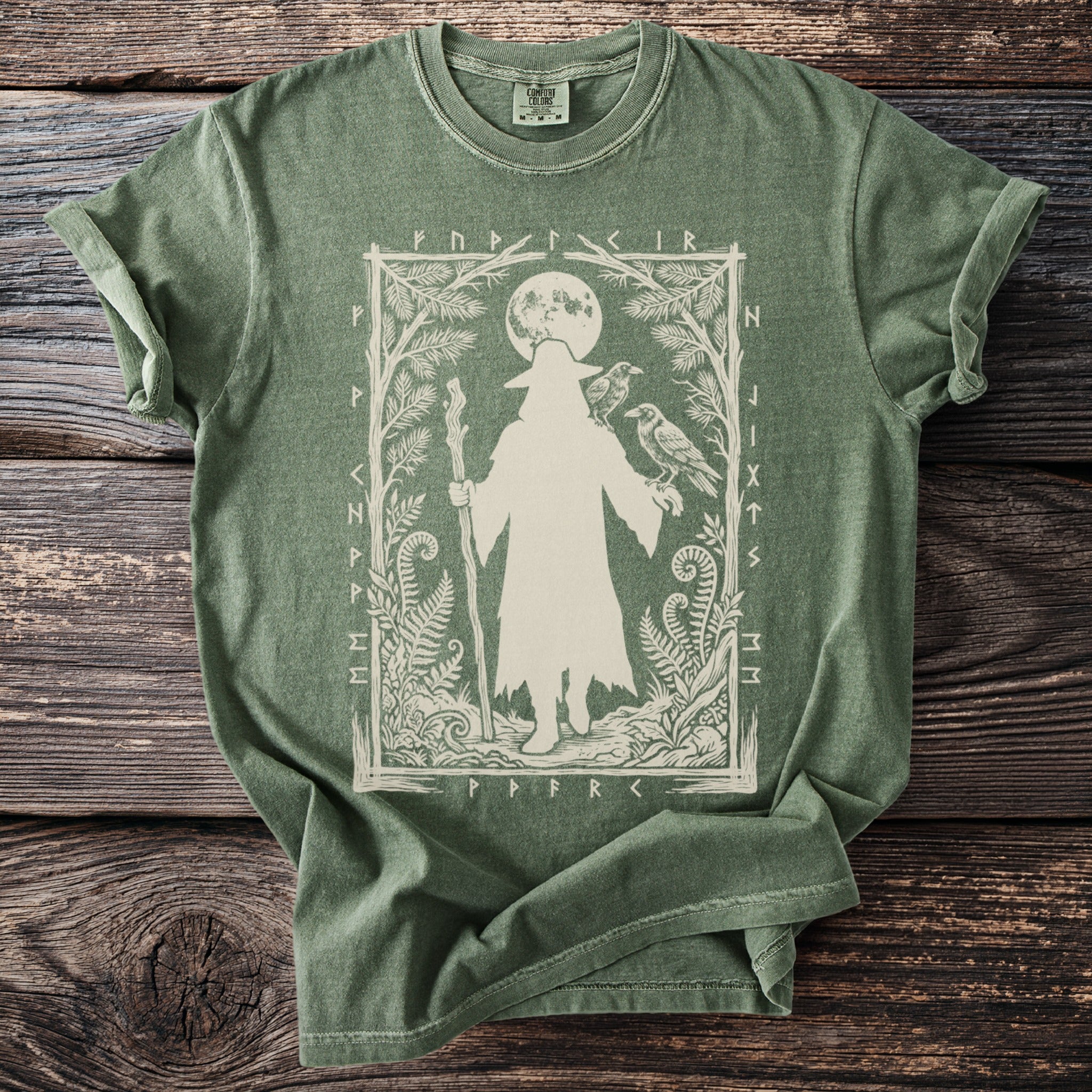 Green t-shirt with cream print of a wizard, two ravens, and runes.