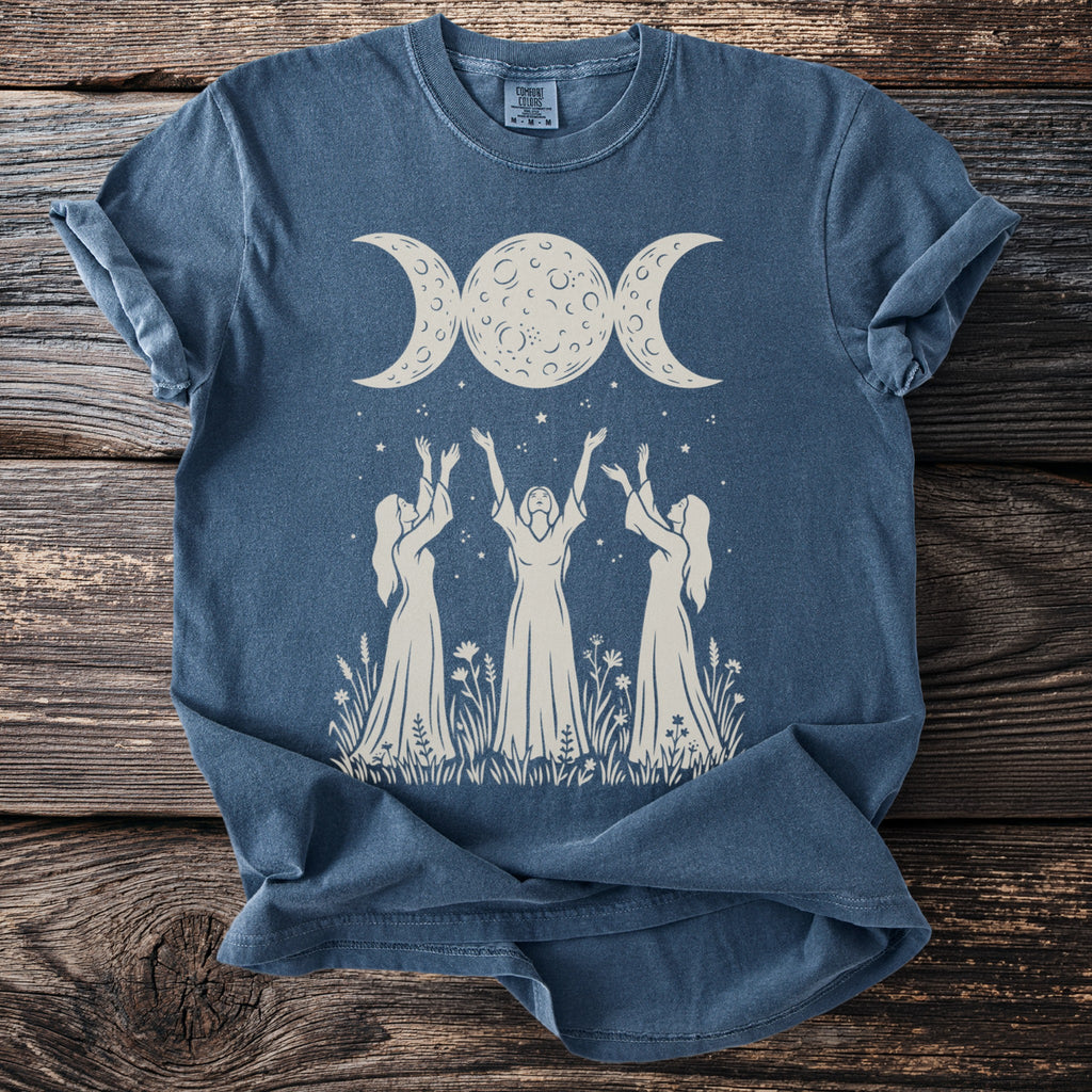 Blue t-shirt with a cream graphic of women reaching for a triple moon.