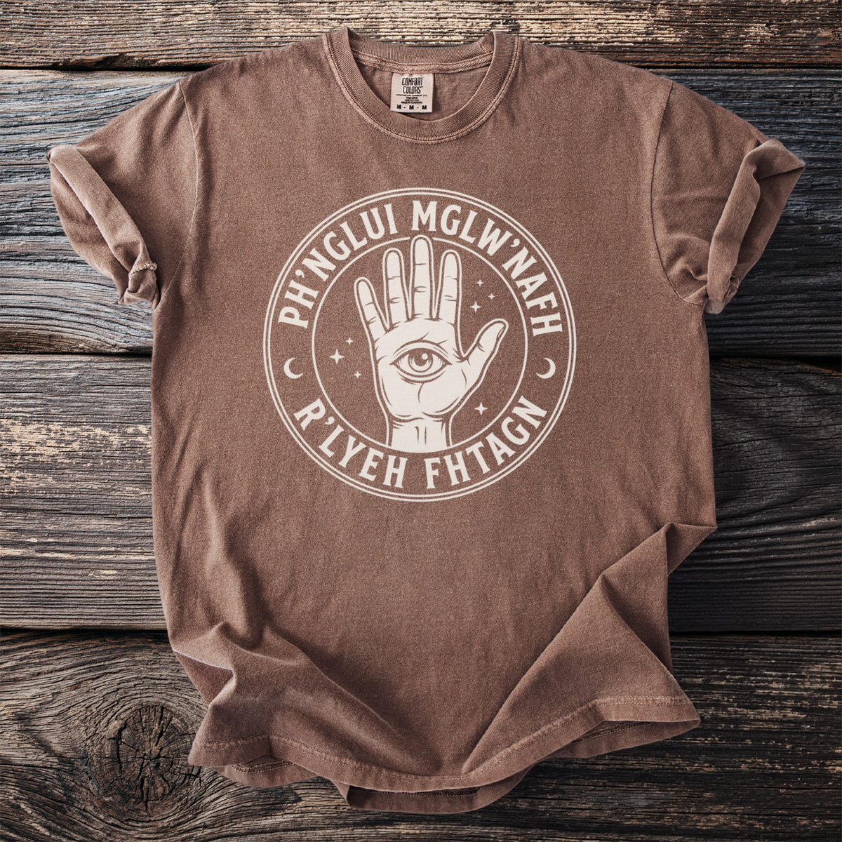 Brown t-shirt with a circular design of an open hand with an eye in the palm.