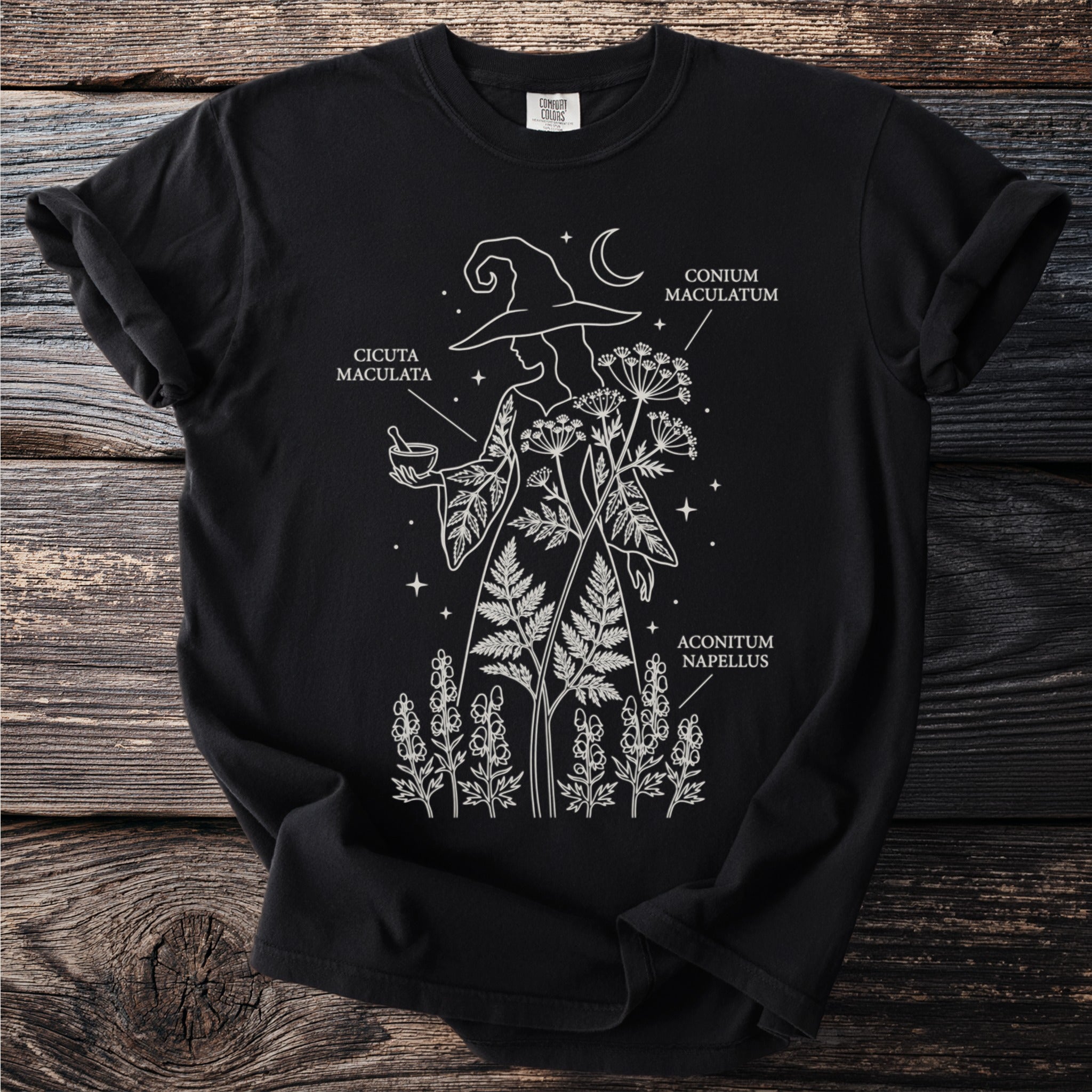 Black t-shirt with a white line drawing of a witch and medicinal plants: Cicuta Maculata, Conium Maculatum, Aconitum Napellus.