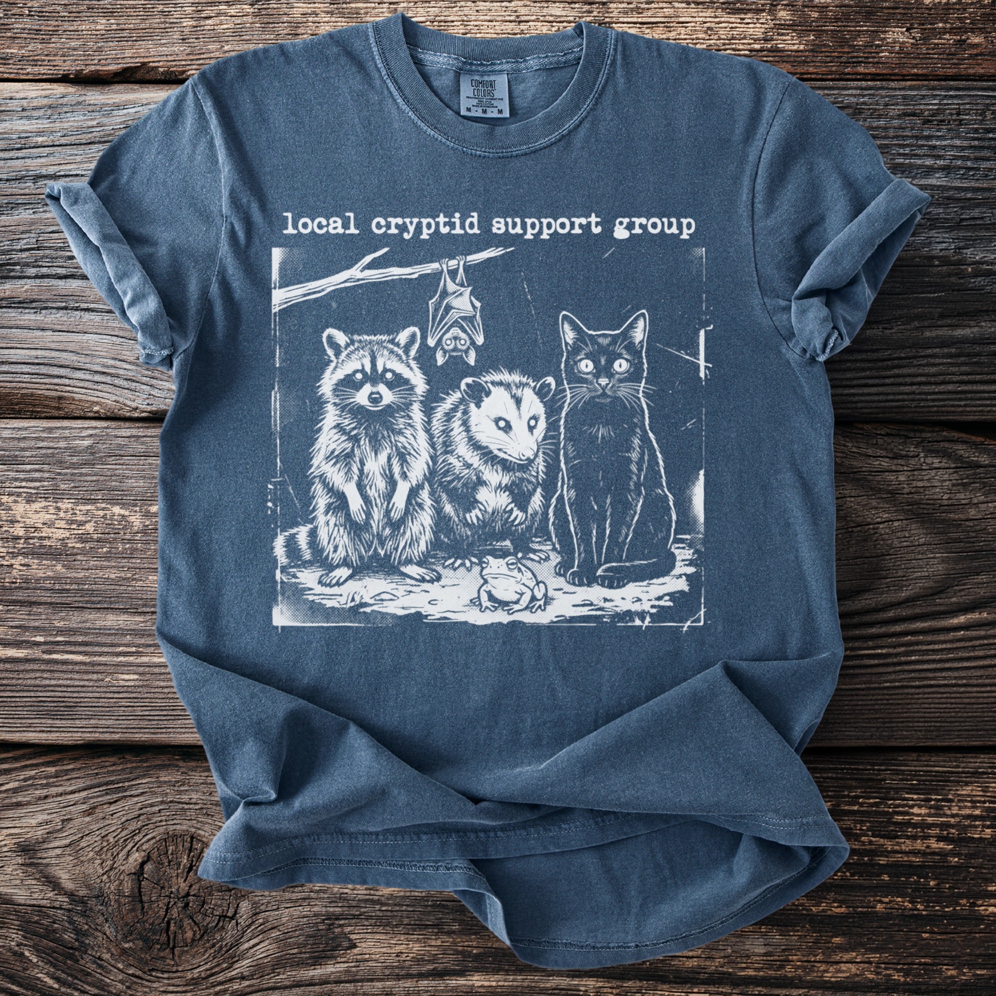 T-shirt with white print of raccoon, possum, black cat, frog, and bat, reading "local cryptid support group."