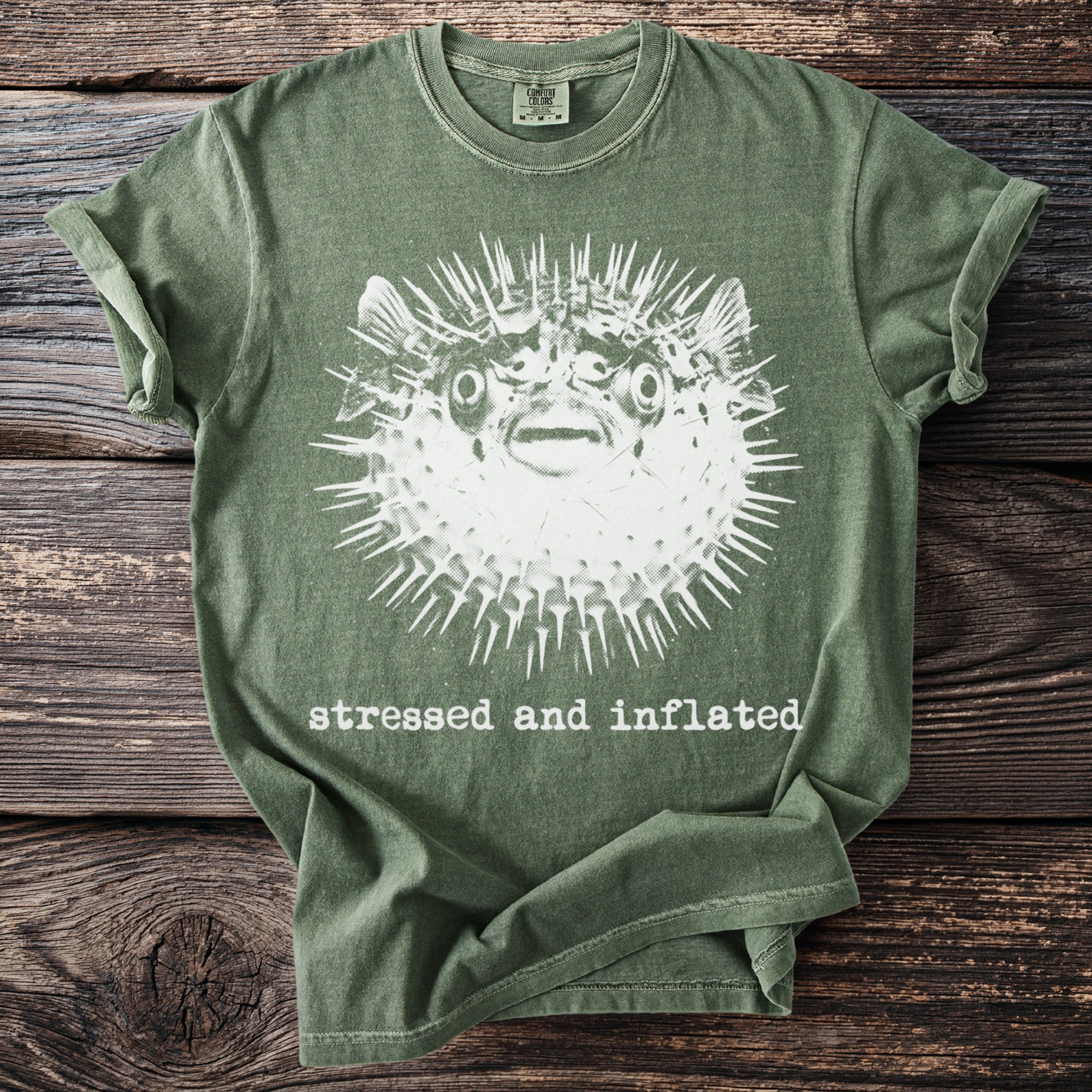 Green t-shirt with a graphic of a spiky pufferfish and text "stressed and inflated."