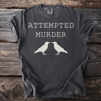 Dark grey t-shirt with white text "ATTEMPTED MURDER" and two crows.