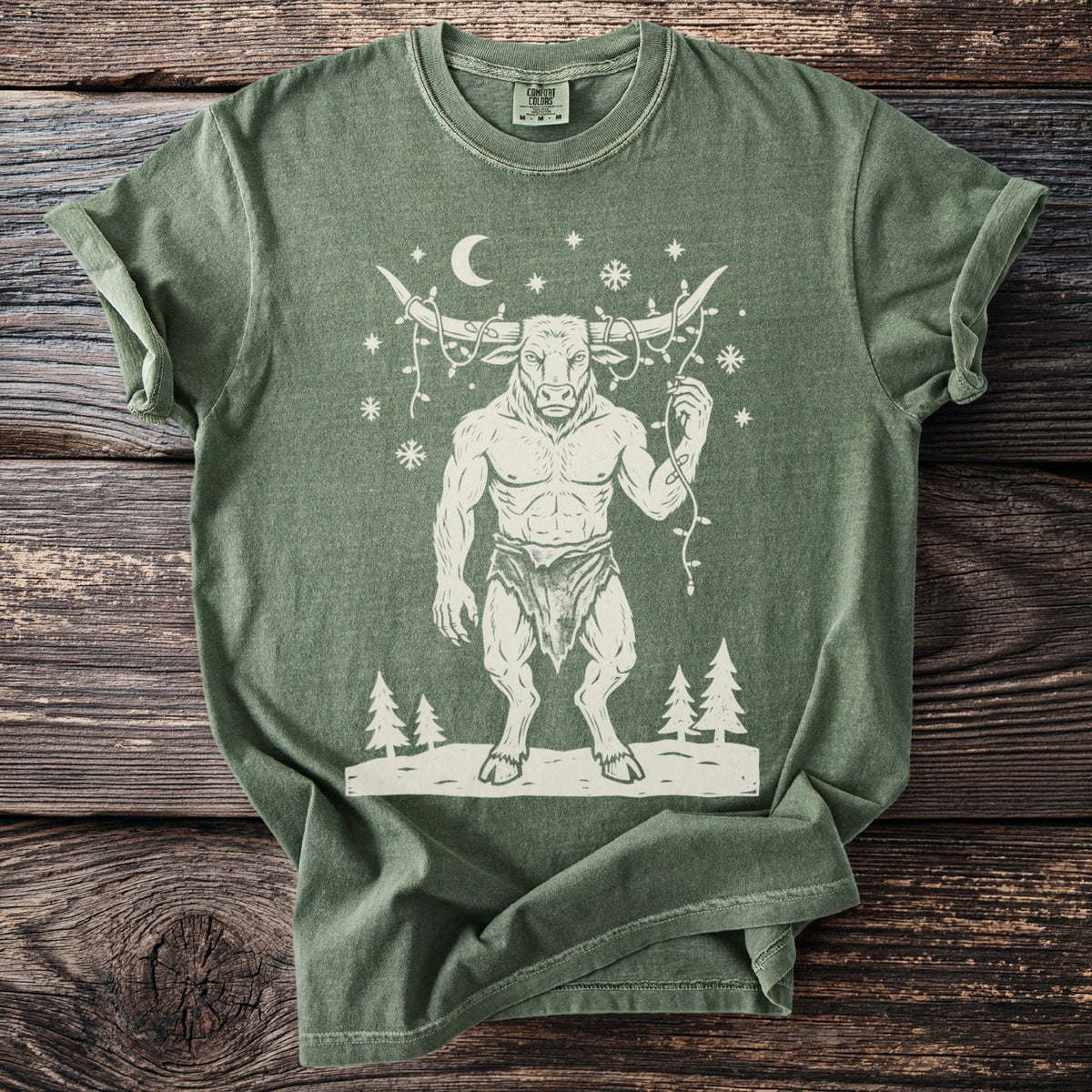 Moss green t-shirt with a cream folk-cut print: the Minotaur stands in the snow with a string of Christmas lights tangled around his horns.