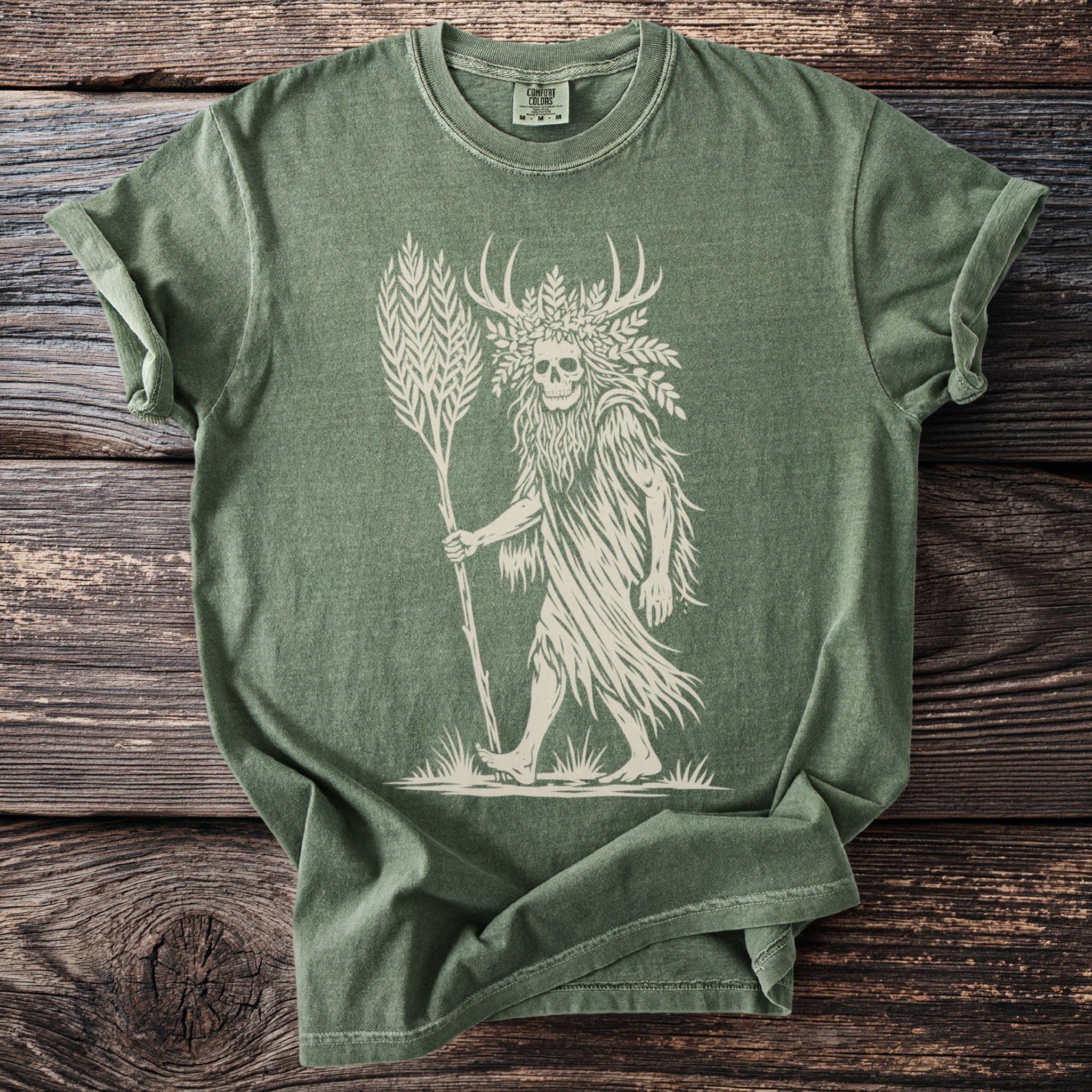Green t-shirt with a cream graphic of a skull-headed figure with antlers and a staff.