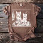 Brown t-shirt with two cats smoking cigarettes and a can of soda on a rug.
