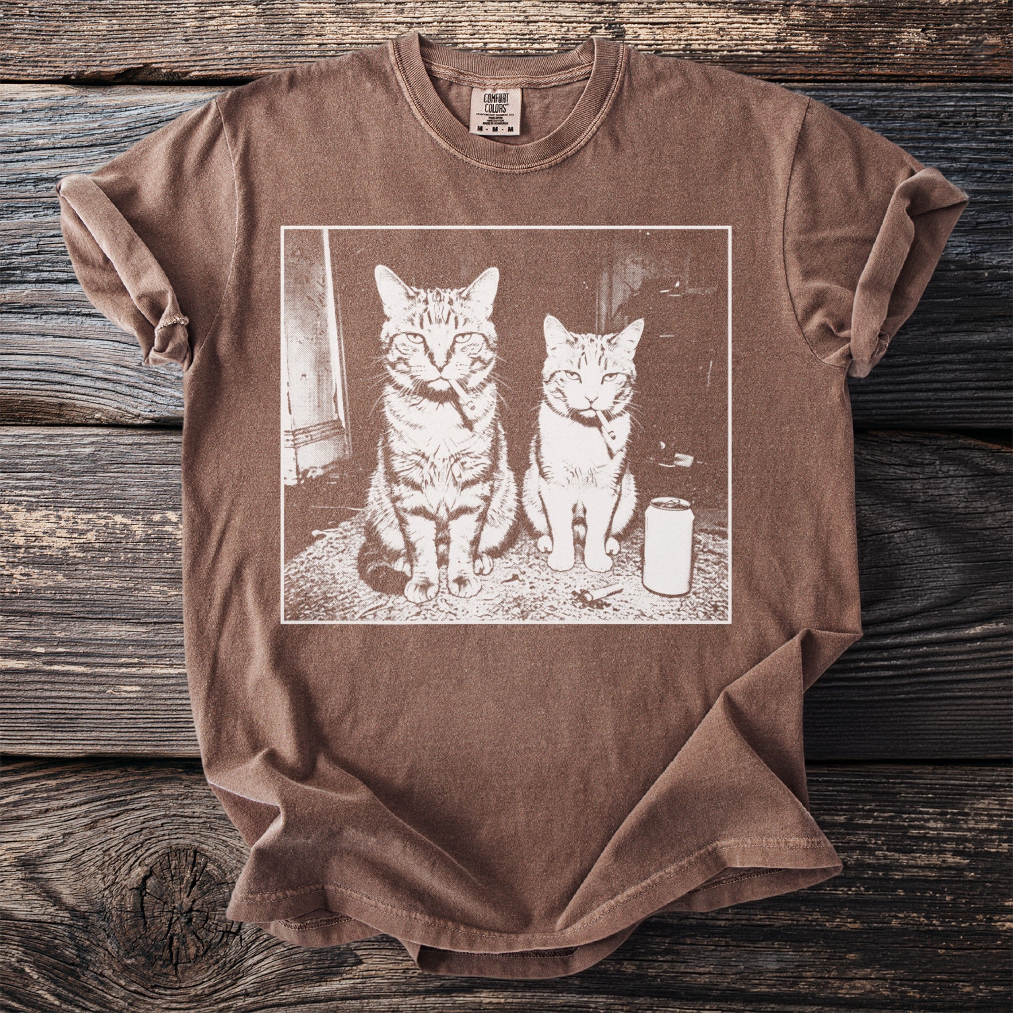 Brown t-shirt with two cats smoking cigarettes and a can of soda on a rug.