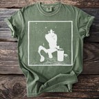 Green t-shirt with a distressed graphic of a black and white cat next to a can.