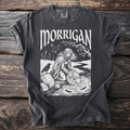Dark gray t-shirt with "MORRIGAN" text and illustration of a woman by a river with a raven.