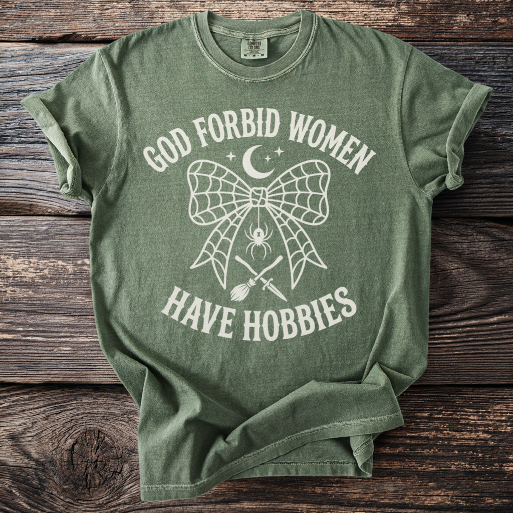 Green t-shirt with white text: "GOD FORBID WOMEN HAVE HOBBIES" graphic.