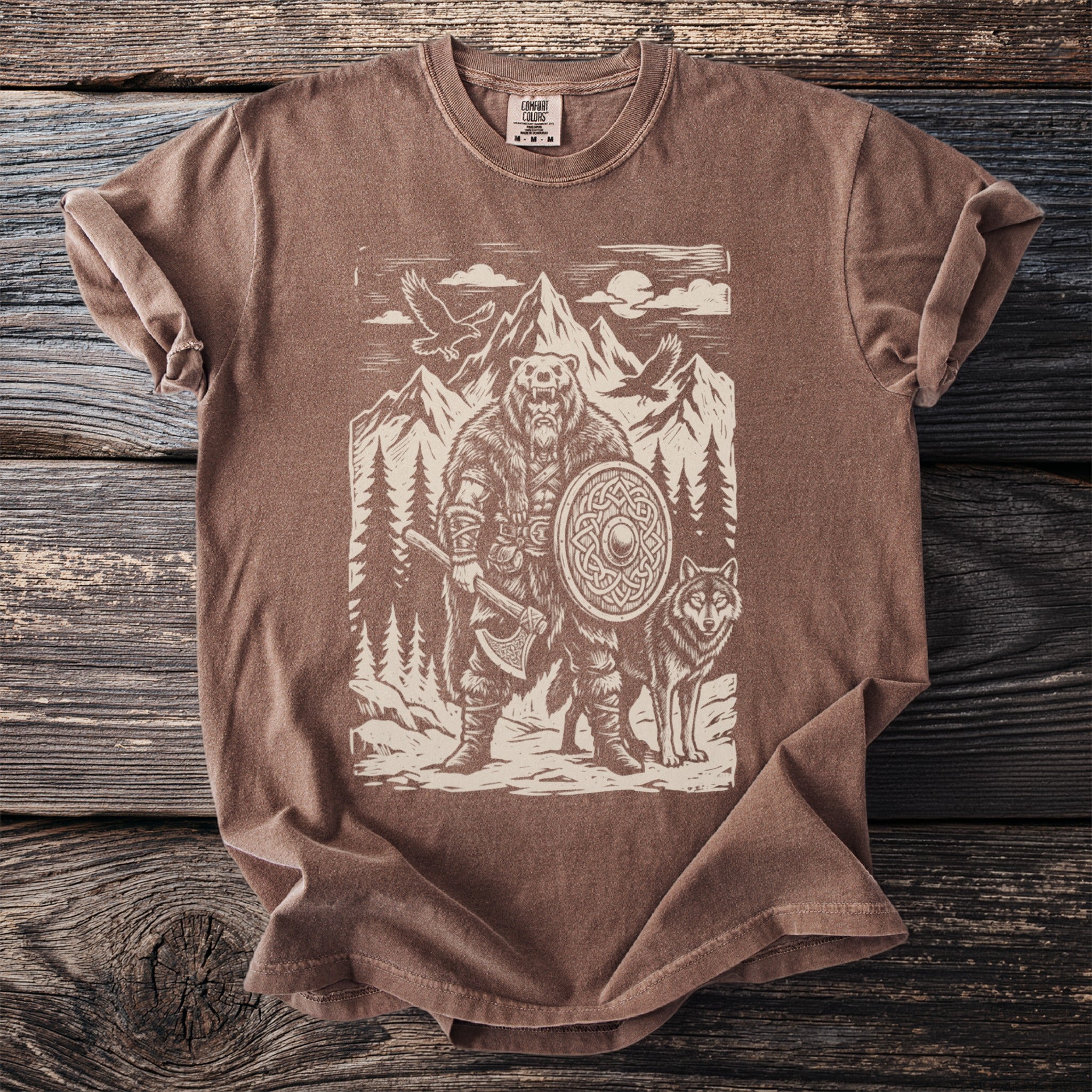 Brown t-shirt with a graphic of a bear warrior, wolf, and mountains.