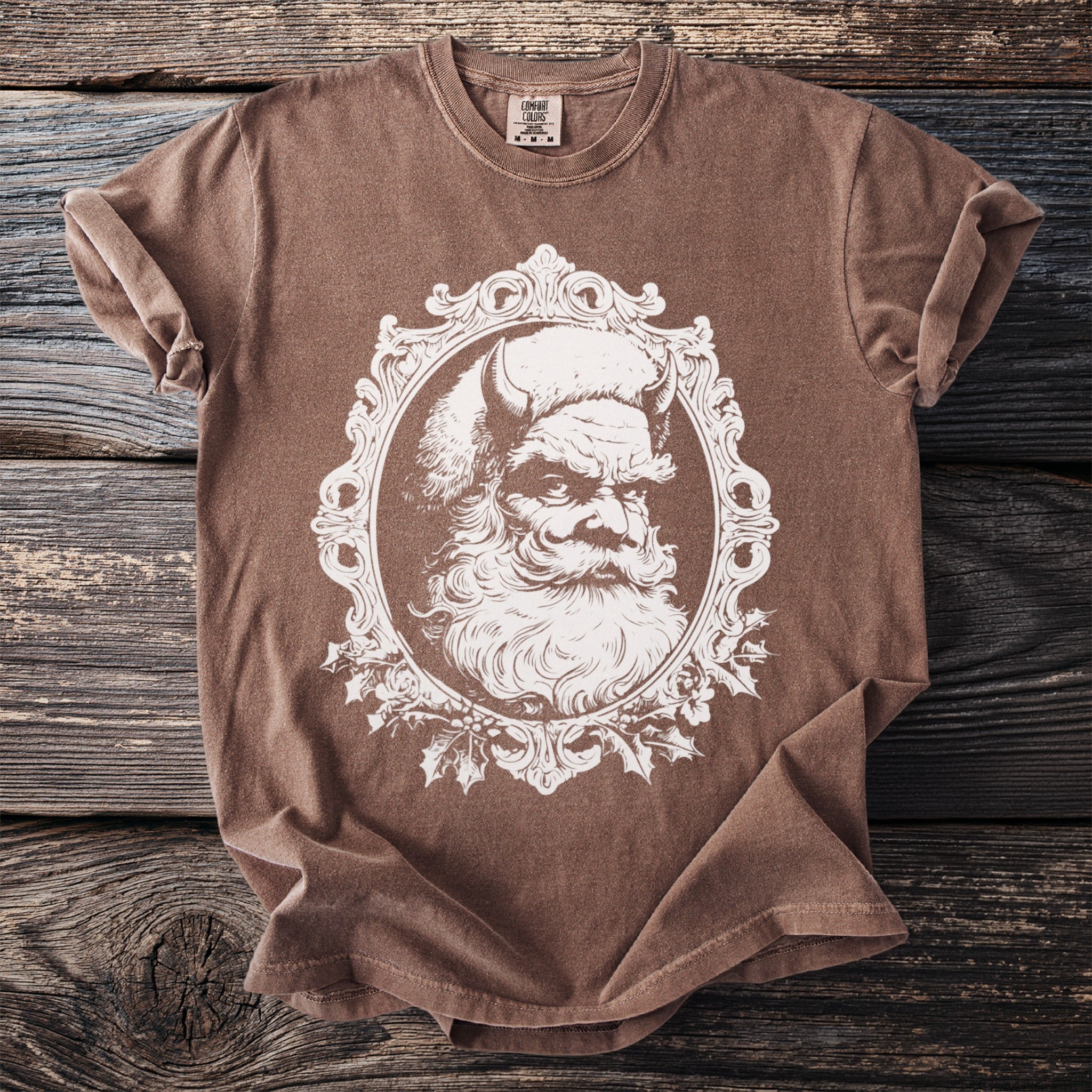 Brown t-shirt with a distressed white illustration of a horned Santa Claus in an ornate frame.