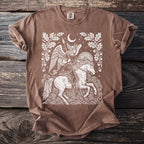 Brown t-shirt with graphic of winged woman on horse under moon surrounded by oak leaves.