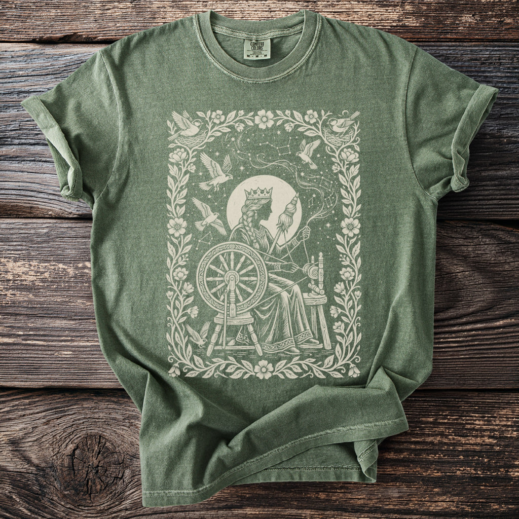 Green t-shirt with a cream-colored print of a queen spinning yarn with birds and constellations.